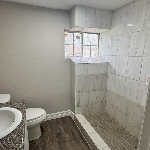 bathroom featuring tiled shower, toilet, baseboards, and wood finished floors