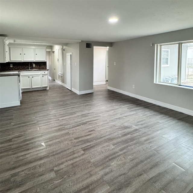 unfurnished living room with a sink, visible vents, baseboards, and dark wood-type flooring