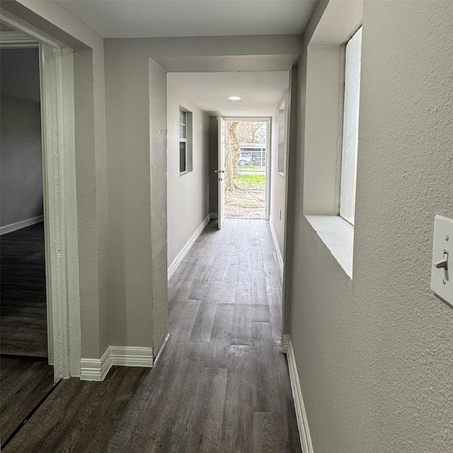 hallway featuring wood finished floors, baseboards, and a textured wall