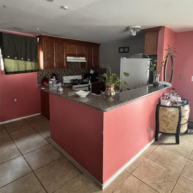 kitchen featuring backsplash, under cabinet range hood, freestanding refrigerator, light tile patterned flooring, and white electric range