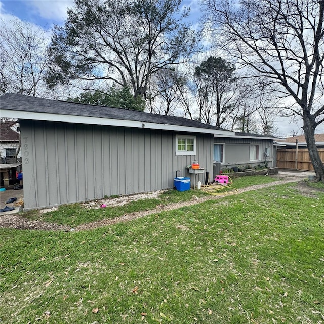 rear view of property featuring a lawn, board and batten siding, and fence