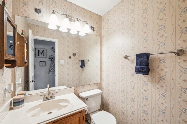 half bath with toilet, wallpapered walls, and vanity