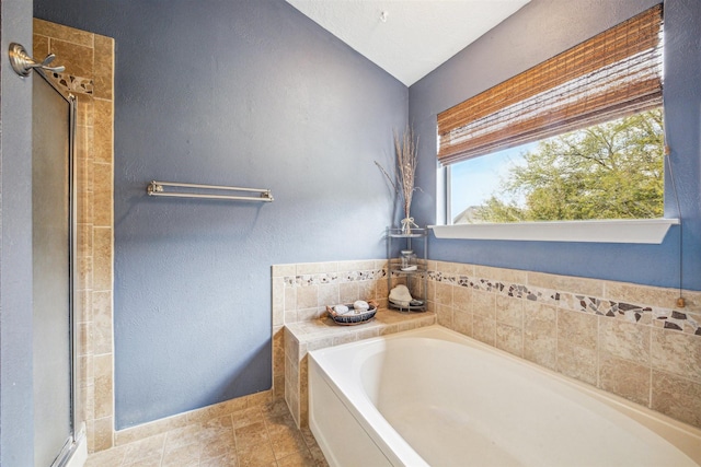 bathroom with tile patterned flooring, a stall shower, a garden tub, and a textured wall