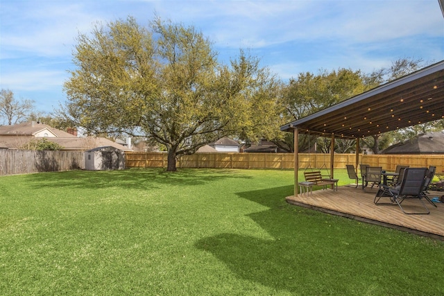 view of yard with a deck, an outdoor structure, a fenced backyard, and a shed