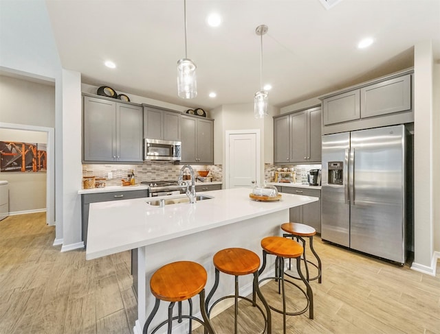 kitchen featuring gray cabinets, appliances with stainless steel finishes, backsplash, light wood finished floors, and a sink