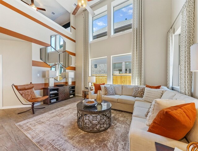 living room with a high ceiling, ceiling fan, wood finished floors, and a healthy amount of sunlight