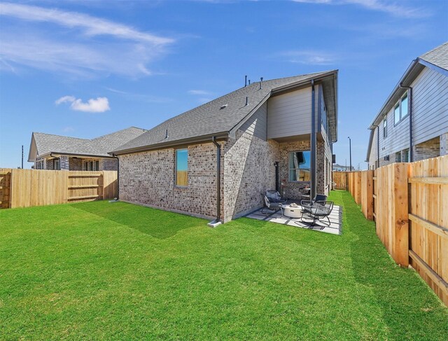 rear view of house with a patio, brick siding, a yard, a fenced backyard, and roof with shingles