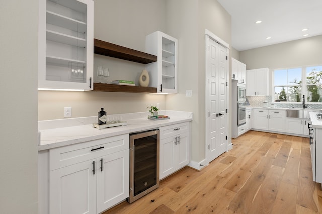 kitchen featuring a sink, stainless steel appliances, wine cooler, light wood-style floors, and white cabinetry