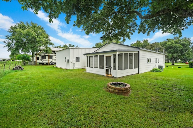 back of property with a yard, a fire pit, and a sunroom