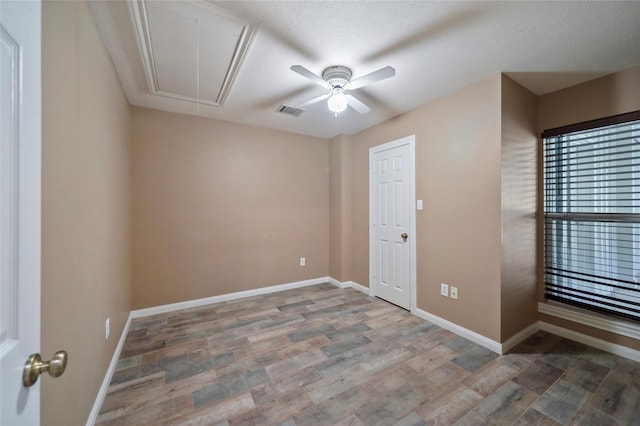 empty room with visible vents, baseboards, attic access, wood finished floors, and a ceiling fan