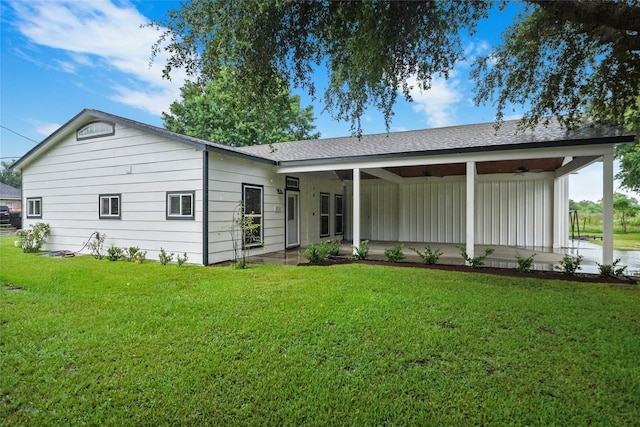 rear view of house with a ceiling fan and a lawn