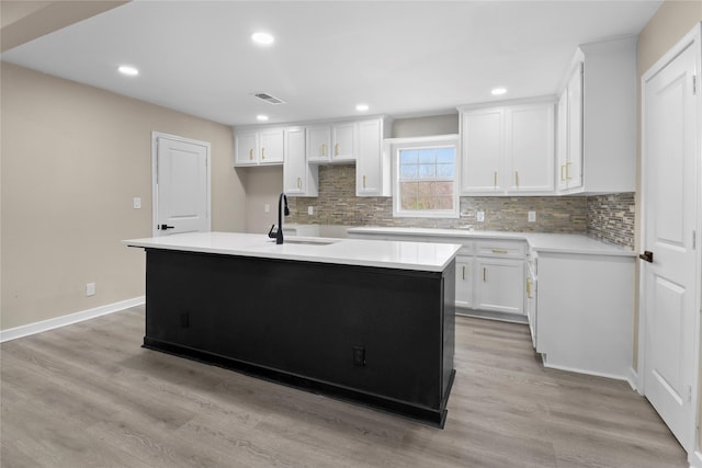 kitchen with a center island with sink, a sink, backsplash, white cabinetry, and light wood finished floors