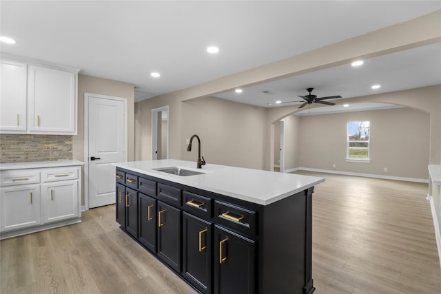 kitchen featuring light wood finished floors, light countertops, arched walkways, white cabinets, and a sink