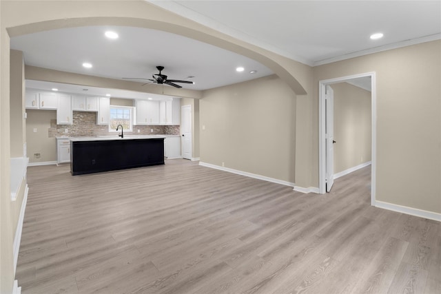 unfurnished living room featuring arched walkways, a ceiling fan, light wood-type flooring, and baseboards