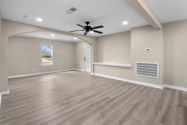 unfurnished living room featuring arched walkways, visible vents, baseboards, and wood finished floors