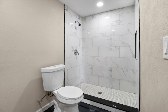 bathroom with toilet, a textured wall, baseboards, and a tile shower