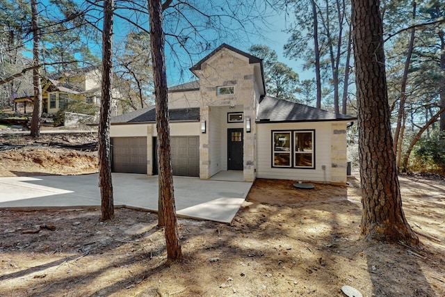 view of front of property featuring concrete driveway, an attached garage, stone siding, and roof with shingles