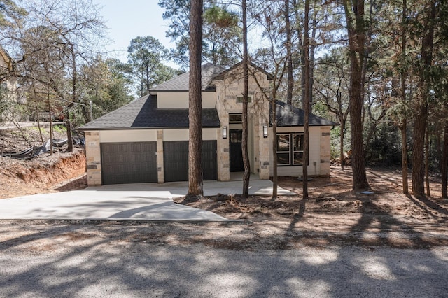 view of front of property with concrete driveway, a garage, stone siding, and roof with shingles