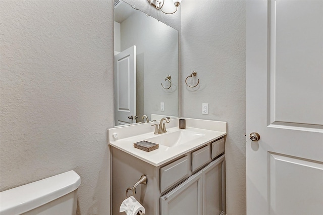 bathroom featuring toilet, vanity, and a textured wall