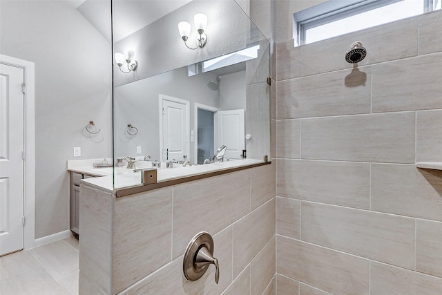 bathroom with vaulted ceiling, double vanity, baseboards, and tiled shower