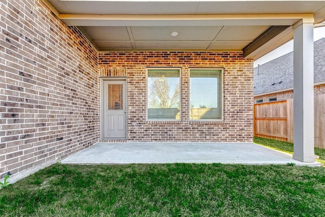 property entrance featuring a patio, brick siding, a lawn, and fence