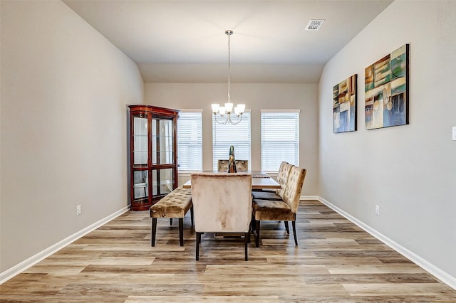 dining room with visible vents, baseboards, lofted ceiling, light wood-style floors, and a notable chandelier