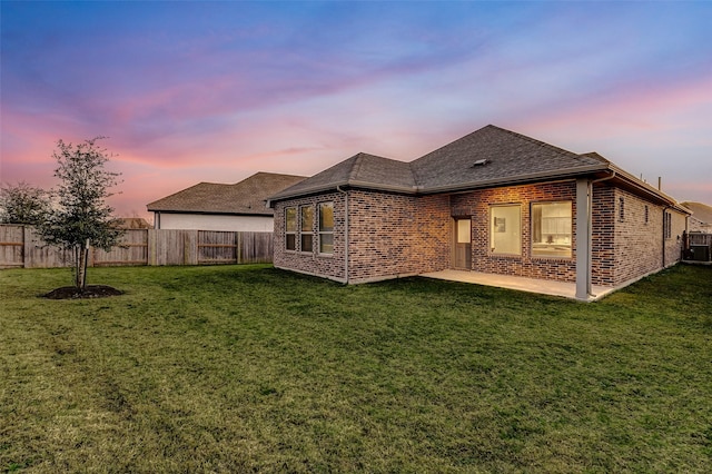 rear view of property with a lawn, roof with shingles, a fenced backyard, and brick siding