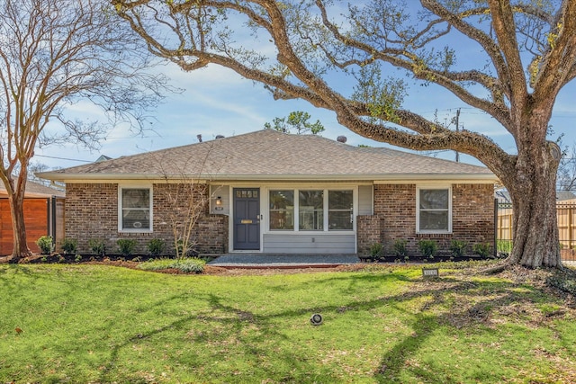 ranch-style home featuring a front lawn, fence, brick siding, and a shingled roof