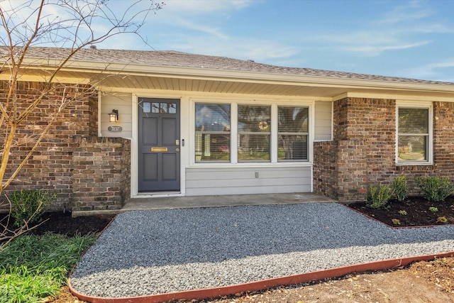 entrance to property with brick siding, a porch, and a shingled roof