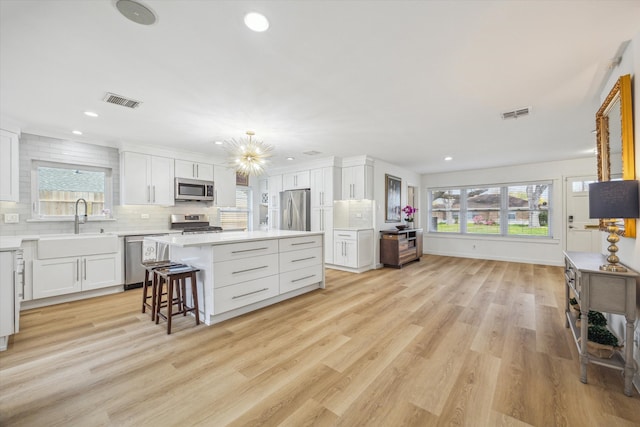 kitchen featuring visible vents, backsplash, a kitchen island, appliances with stainless steel finishes, and a sink