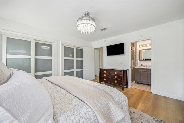 bedroom featuring visible vents, connected bathroom, light wood finished floors, baseboards, and a chandelier