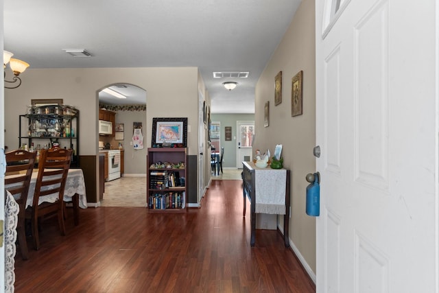 interior space with dark wood-type flooring, visible vents, arched walkways, and baseboards