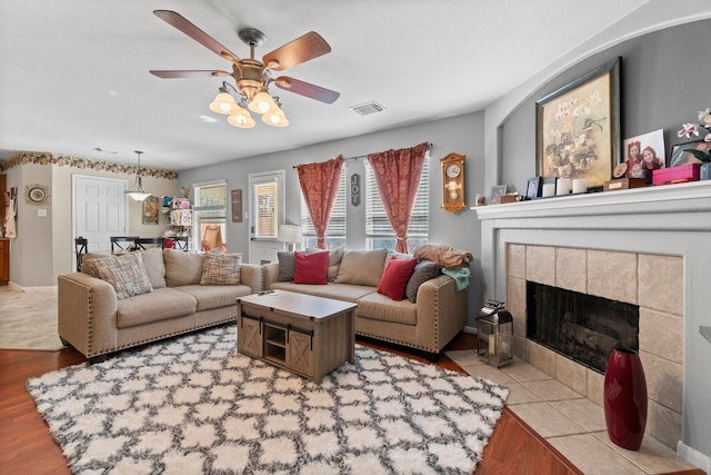 living room featuring a tiled fireplace, visible vents, ceiling fan, and wood finished floors