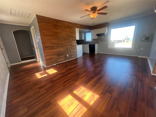 unfurnished living room featuring visible vents, dark wood-type flooring, a ceiling fan, arched walkways, and baseboards