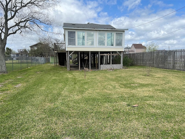 rear view of property featuring a shingled roof, stairs, a sunroom, a fenced backyard, and a yard