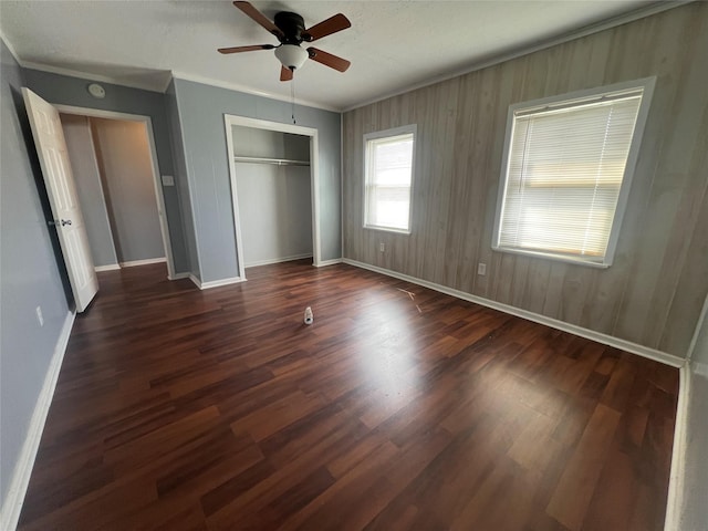 unfurnished bedroom featuring a ceiling fan, dark wood-style floors, a closet, crown molding, and baseboards