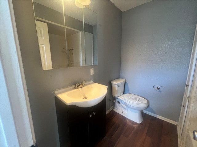 bathroom with vanity, toilet, wood finished floors, and baseboards