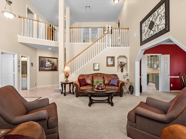 carpeted living area featuring stairway, baseboards, a high ceiling, and visible vents