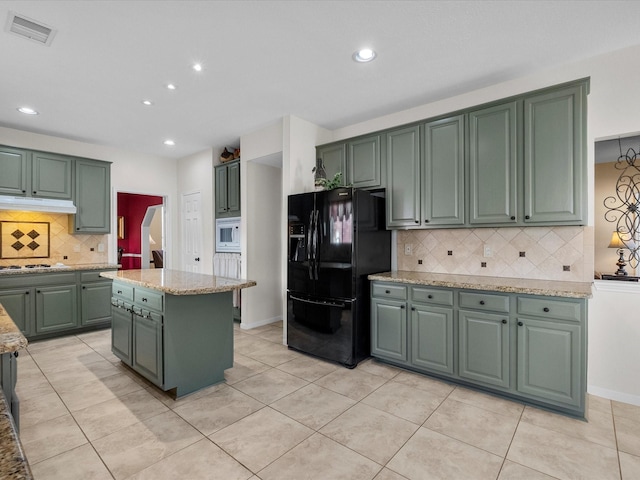 kitchen featuring white microwave, visible vents, green cabinets, light stone counters, and black fridge