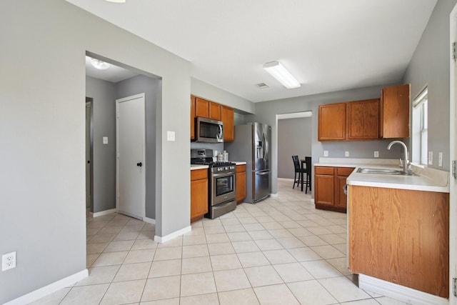 kitchen with brown cabinetry, light tile patterned flooring, a sink, stainless steel appliances, and light countertops