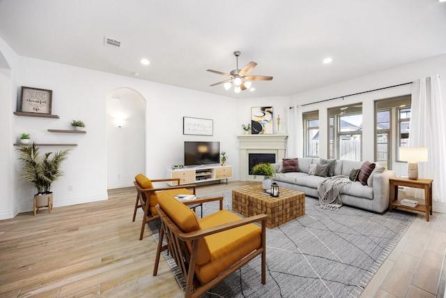 living room with visible vents, light wood-style flooring, recessed lighting, arched walkways, and a fireplace