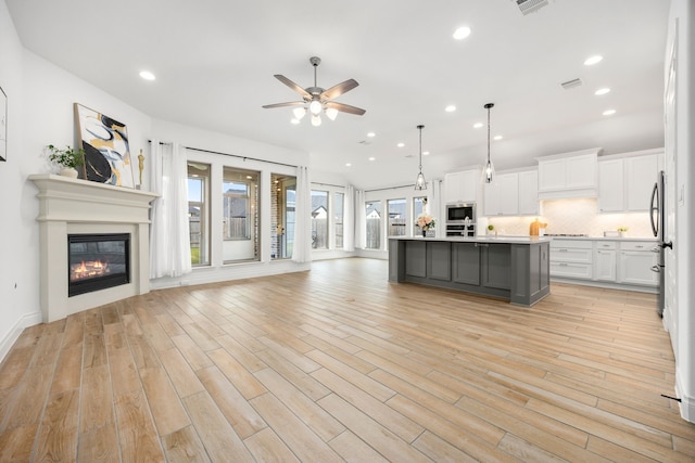 kitchen with backsplash, open floor plan, light countertops, a glass covered fireplace, and white cabinets