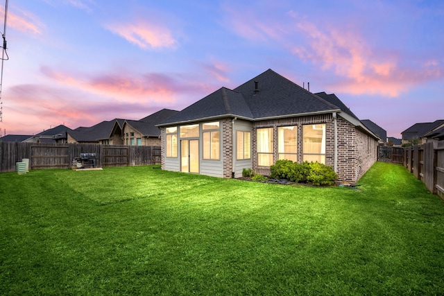 back of property at dusk with a yard, a fenced backyard, and brick siding