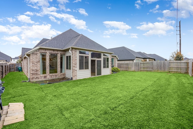 rear view of property featuring brick siding, a fenced backyard, a lawn, and roof with shingles