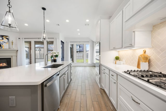 kitchen with a sink, a glass covered fireplace, appliances with stainless steel finishes, light countertops, and decorative backsplash