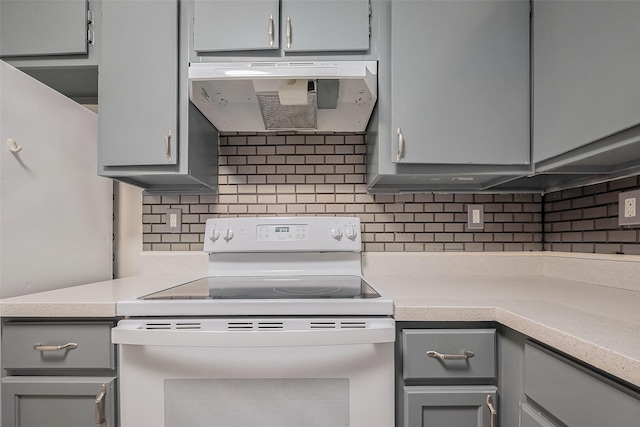 kitchen with under cabinet range hood, gray cabinets, white electric stove, and tasteful backsplash