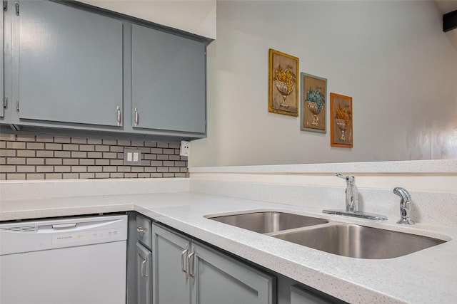 kitchen featuring white dishwasher, a sink, decorative backsplash, light countertops, and gray cabinetry