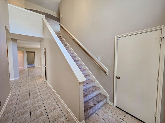 stairway with baseboards, a towering ceiling, and tile patterned flooring