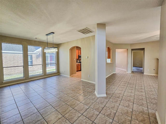 unfurnished room featuring visible vents, baseboards, light tile patterned floors, arched walkways, and a textured ceiling