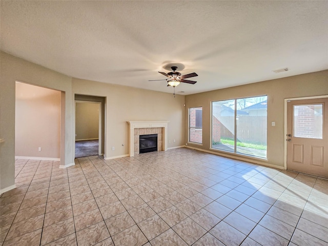 unfurnished living room with a tiled fireplace, baseboards, visible vents, and ceiling fan